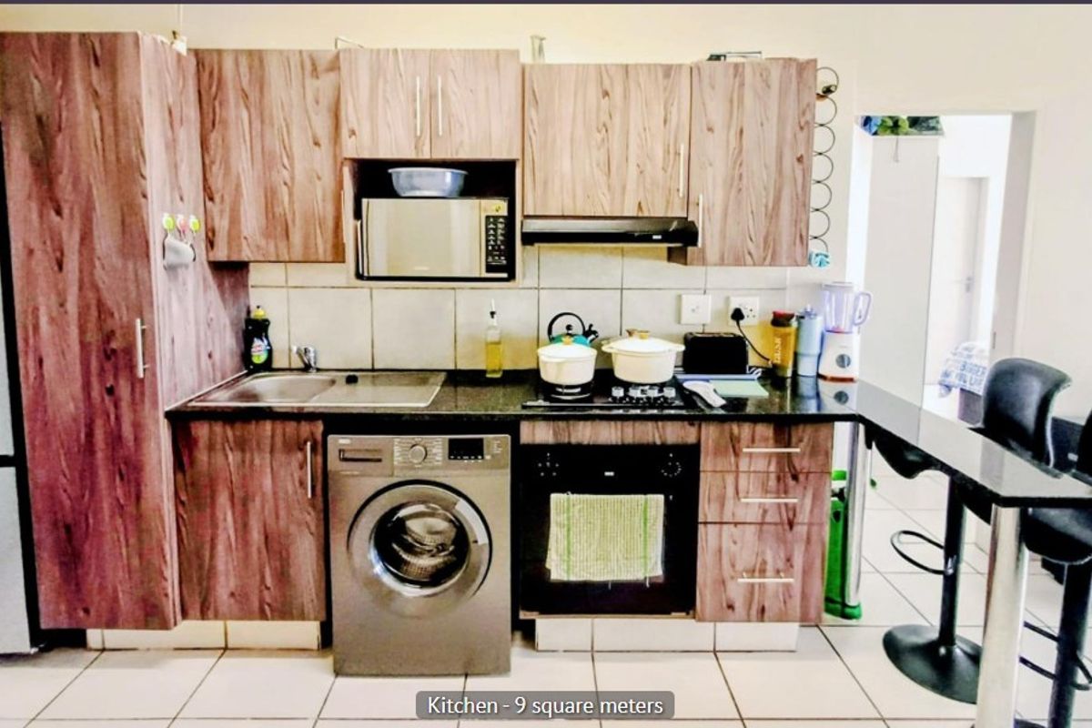 Compact kitchen featuring wood-look laminate cabinetry, granite countertops, built-in oven, hob, extractor fan, and integrated laundry appliance space.