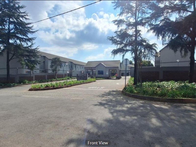 Front view of the apartment complex entrance featuring a paved driveway, security gate, guard house, and established perimeter landscaping.