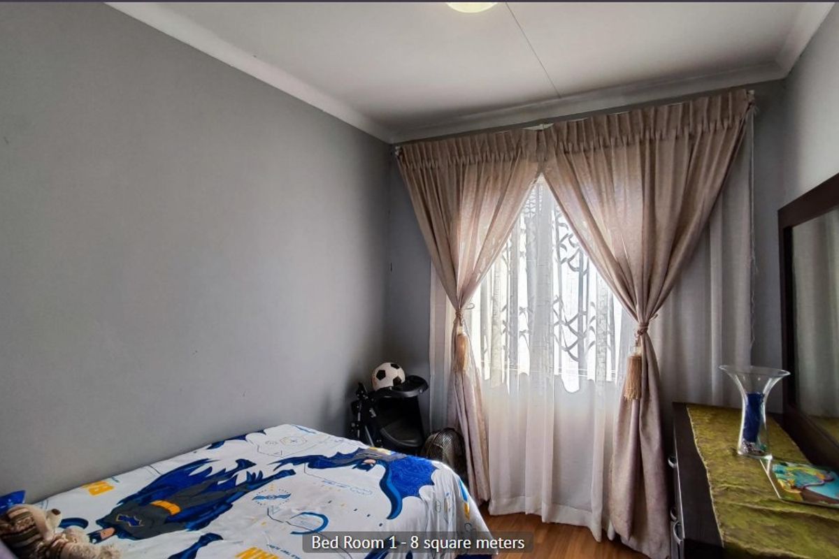 A compact bedroom featuring laminate flooring, neutral grey walls, and window treatments, offering a functional space for a single bed or home office setup.