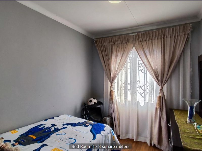 A compact bedroom featuring laminate flooring, neutral grey walls, and window treatments, offering a functional space for a single bed or home office setup.