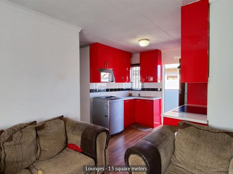Open plan living area featuring a compact kitchen with vibrant red cabinetry, integrated hob, and laminate flooring.