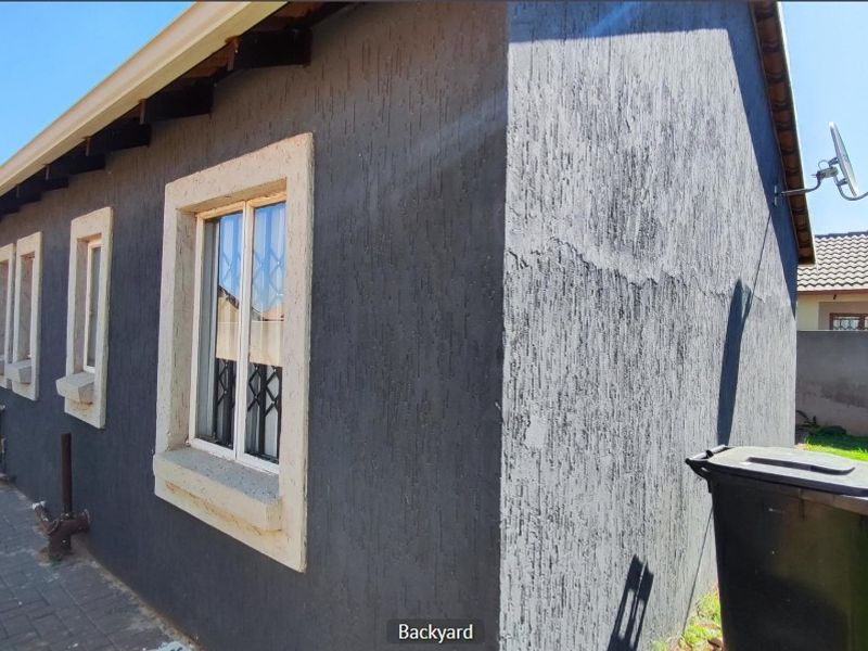 Rear exterior view of the house featuring dark textured wall finishes, security bars on windows, and a paved side walkway.
