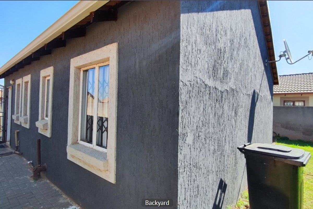 Rear exterior view of the house featuring dark textured wall finishes, security bars on windows, and a paved side walkway.