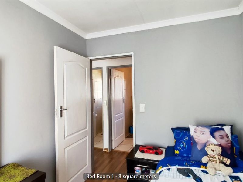 A compact bedroom featuring laminate flooring, neutral grey walls, and direct access to an adjoining room.