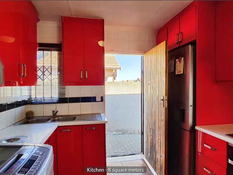 Compact kitchen featuring vibrant red cabinetry, tiled backsplash, built-in oven, extractor fan, and direct access to the exterior.