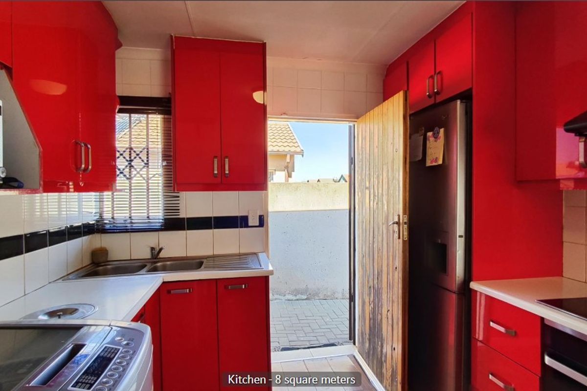Compact kitchen featuring vibrant red cabinetry, tiled backsplash, built-in oven, extractor fan, and direct access to the exterior.