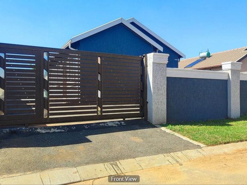 Front view of the property featuring a modern sliding gate, secure boundary wall with concrete pillars, and a paved driveway entrance.
