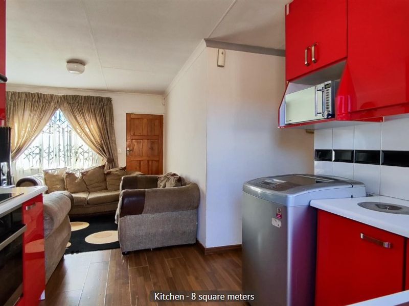 Open-plan kitchen and living area featuring vibrant red cabinetry, modern laminate flooring, and integrated kitchen appliances.