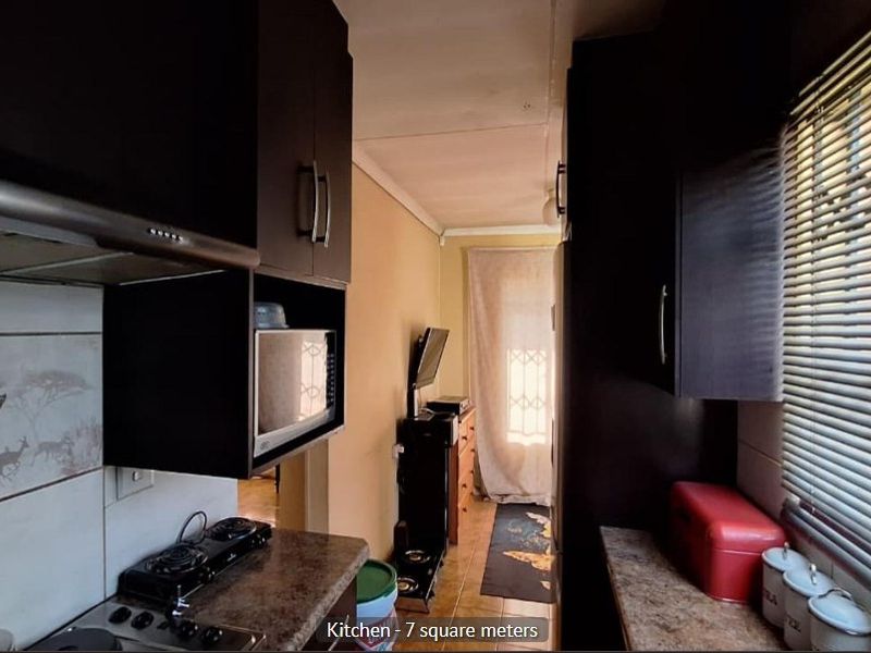 Compact galley-style kitchen featuring dark cabinetry, laminate countertops, and integrated appliances, providing a functional workspace with natural light from the side window.