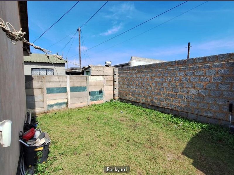 A private backyard area featuring a grass lawn enclosed by a combination of precast concrete and unfinished block boundary walls.