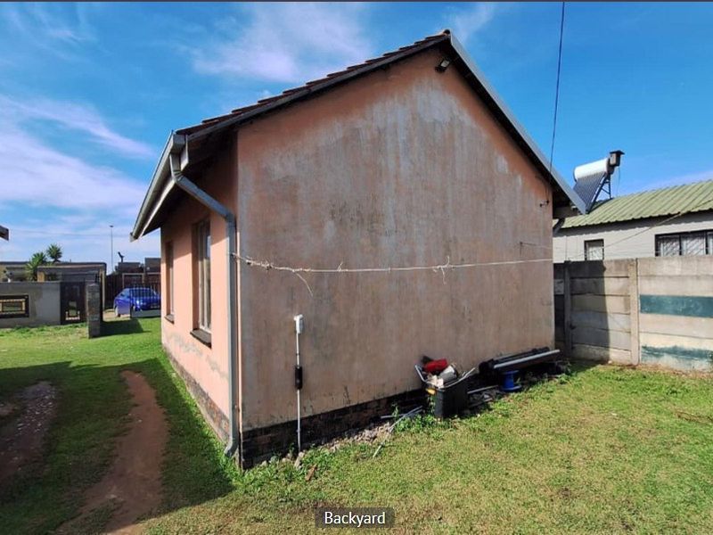 Rear view of the property showing the exterior wall, tiled roof, solar water heater, and surrounding garden area with precast boundary walling.