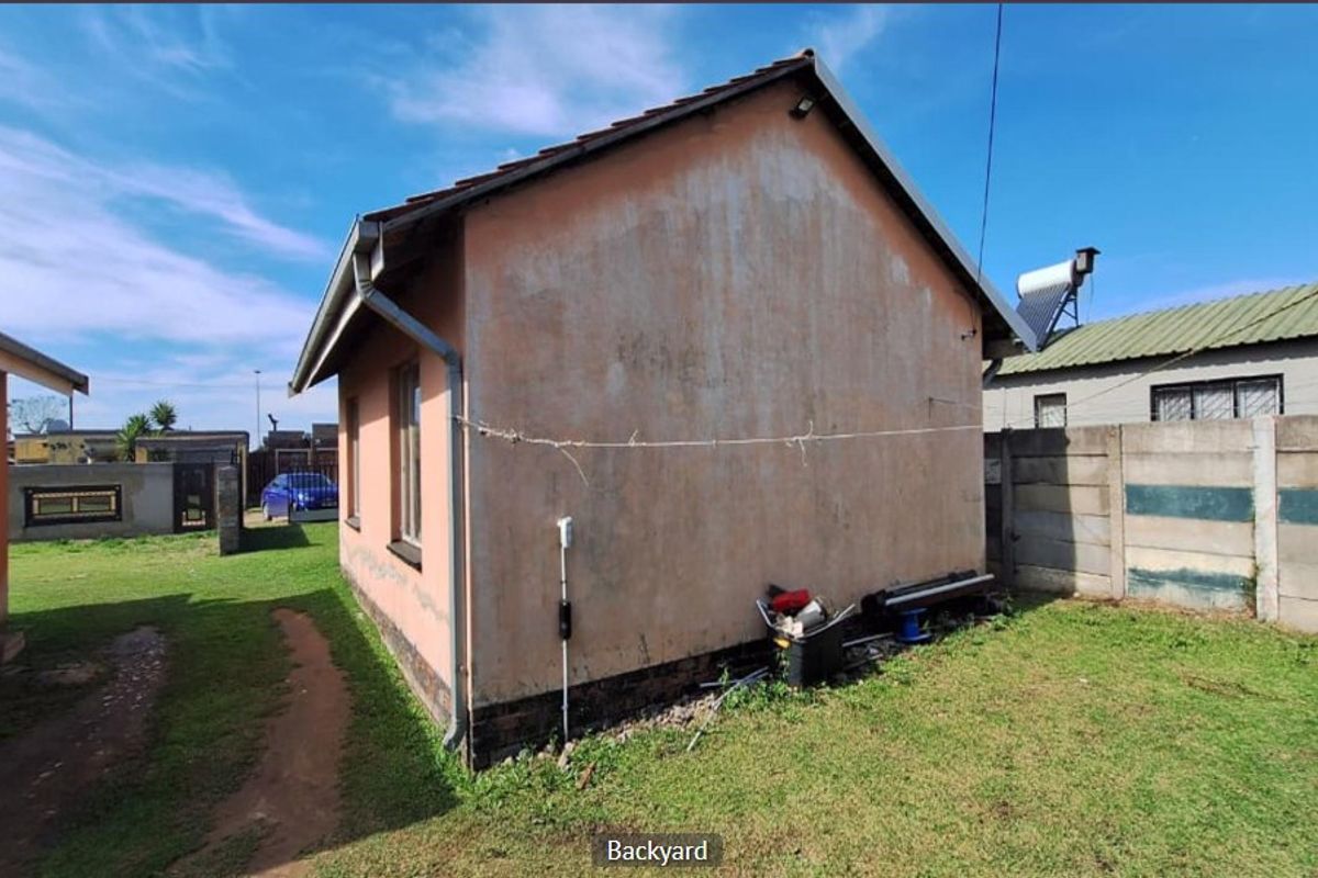 Rear view of the property showing the exterior wall, tiled roof, solar water heater, and surrounding garden area with precast boundary walling.