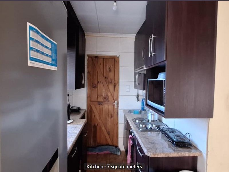 Compact galley-style kitchen featuring dark built-in cabinetry, laminate countertops, a gas hob, and a rustic timber door.