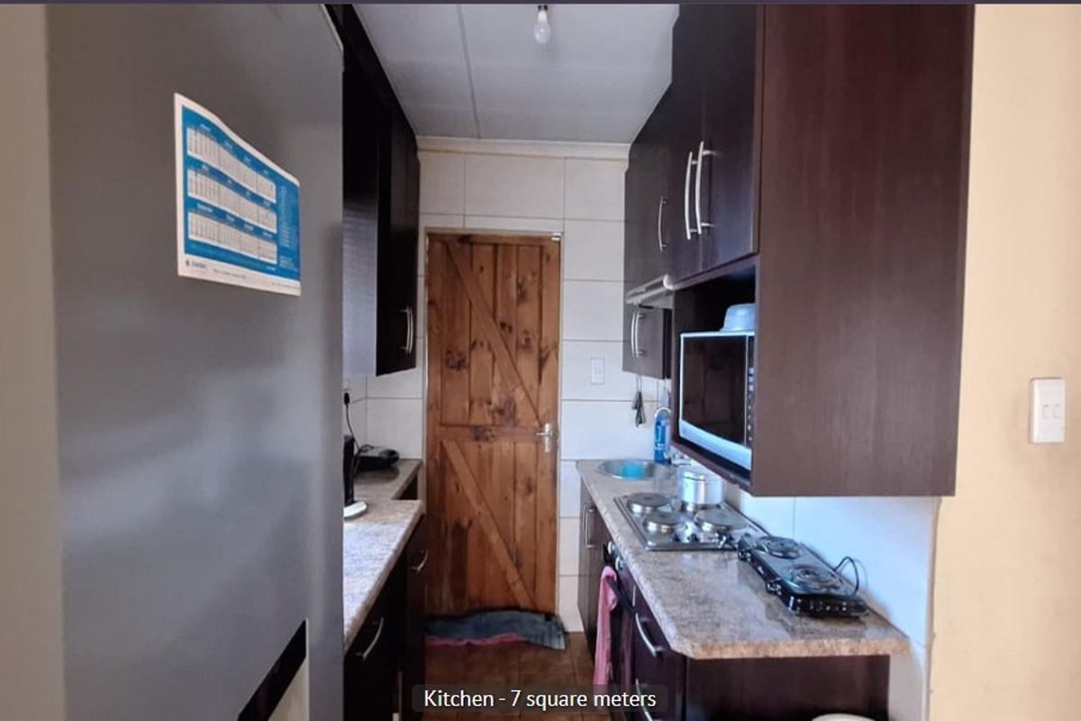 Compact galley-style kitchen featuring dark built-in cabinetry, laminate countertops, a gas hob, and a rustic timber door.