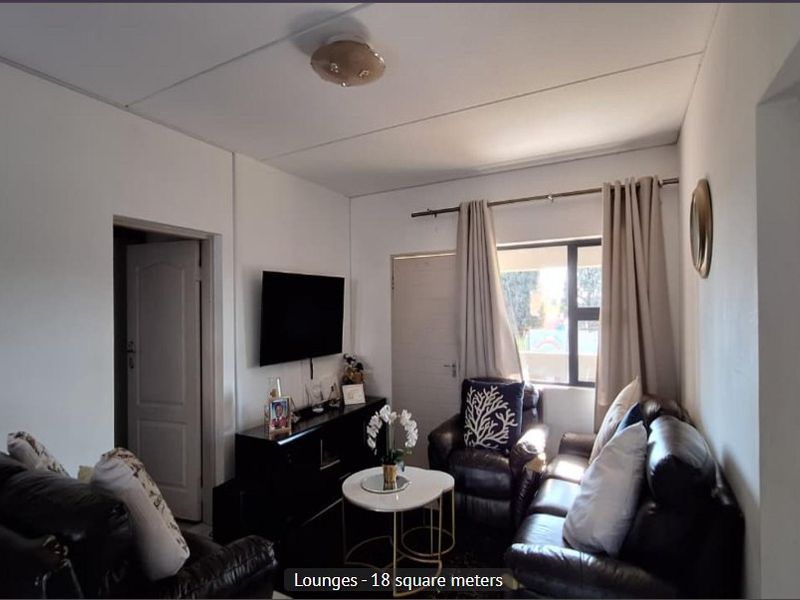 A compact living room featuring neutral walls, a window with curtains, and standard interior door access.