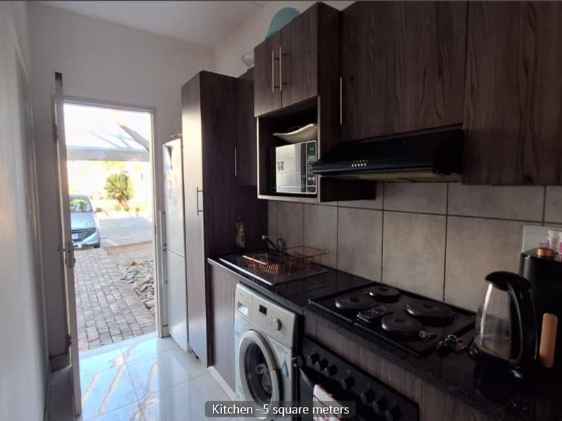 Compact kitchen featuring dark wood cabinetry, granite countertops, built-in electric hob, extractor fan, and tiled flooring with direct access to the exterior.