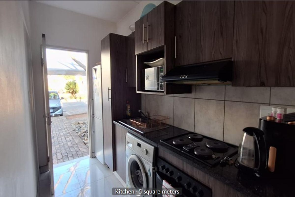 Compact kitchen featuring dark wood cabinetry, granite countertops, built-in electric hob, extractor fan, and tiled flooring with direct access to the exterior.
