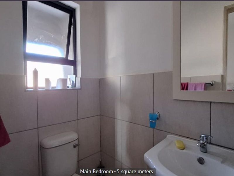 A compact bathroom featuring neutral wall tiling, a pedestal basin, a toilet, and a framed mirror.
