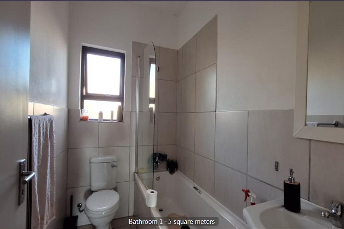 A functional bathroom featuring a bathtub with a glass screen, a wall-mounted basin, and neutral wall tiling.