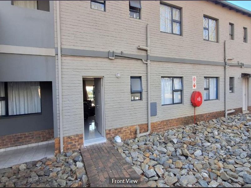 Front exterior view of an apartment building featuring a brick facade, casement windows, and a paved entrance walkway.