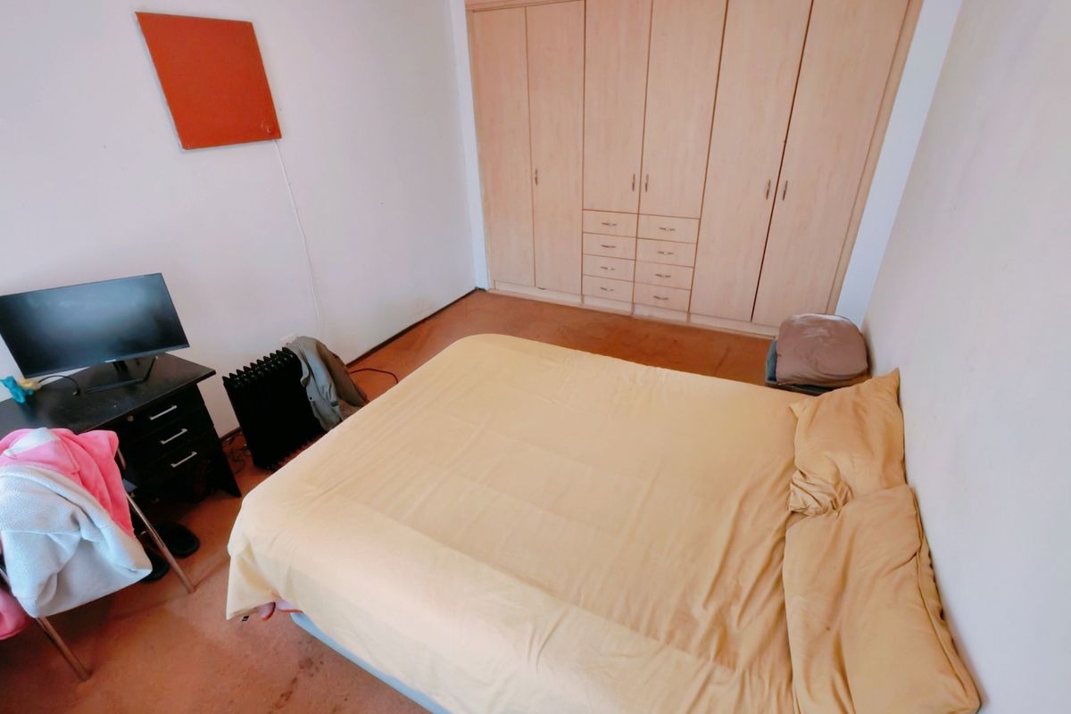 A functional bedroom featuring built-in wooden cupboards and carpeted flooring, offering a practical layout for comfortable living.