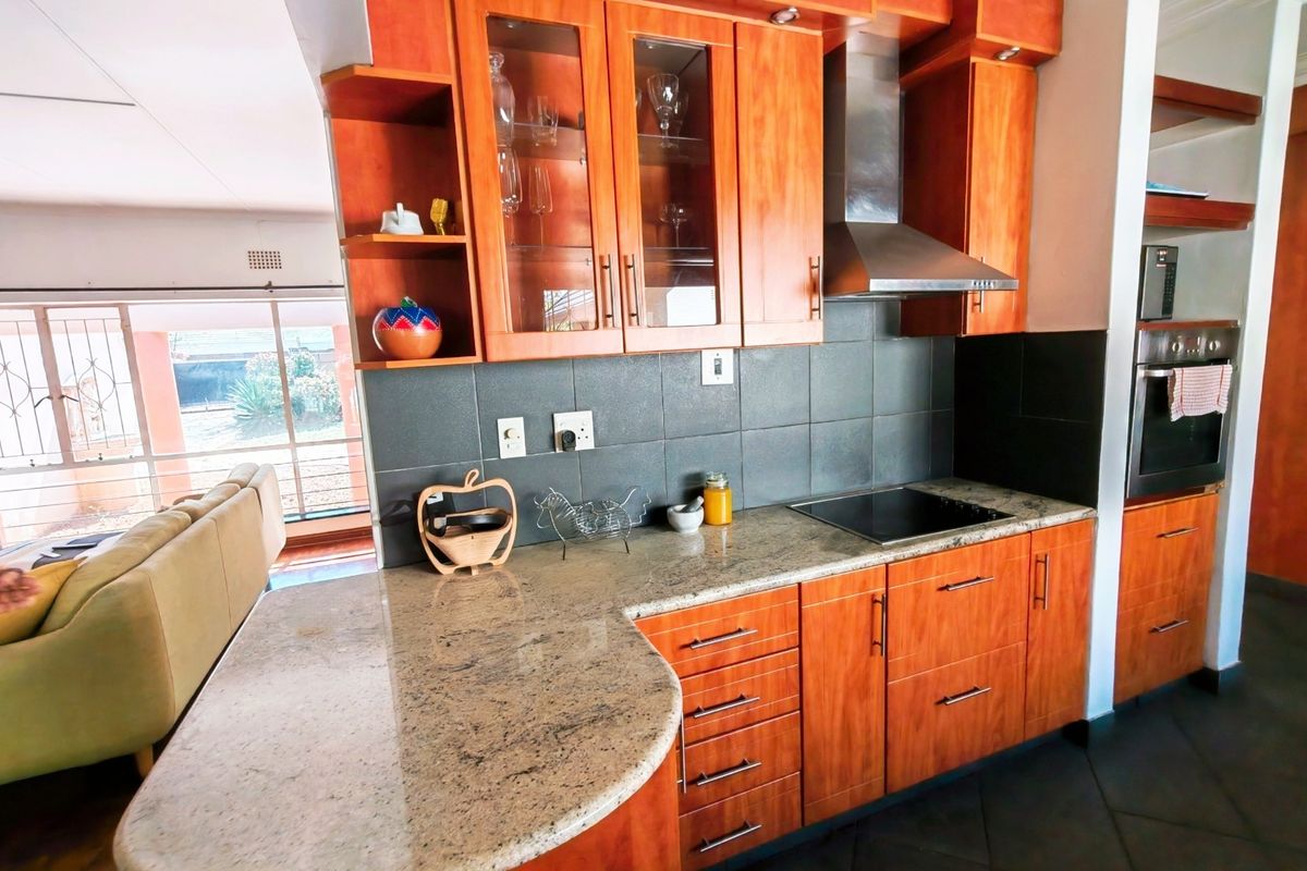 A well-maintained kitchen featuring warm-toned wooden cabinetry, granite countertops, a built-in oven, and a modern stainless steel extractor fan.