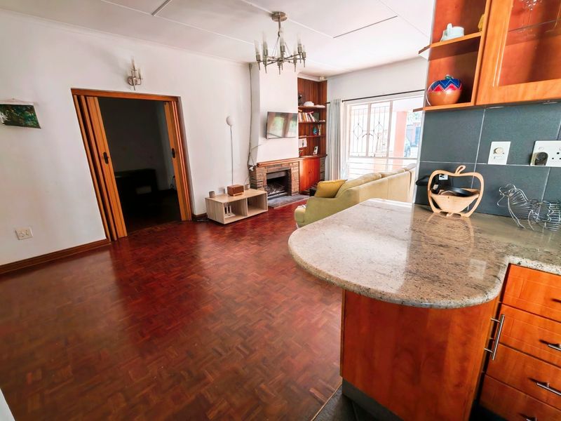 Open plan living area featuring parquet flooring, a brick fireplace with built-in shelving, and a kitchen with granite countertops and wooden cabinetry.
