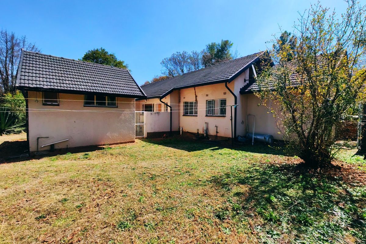 Rear view of the house showing the backyard, tiled roof, and plastered exterior walls with some visible wear and maintenance requirements.