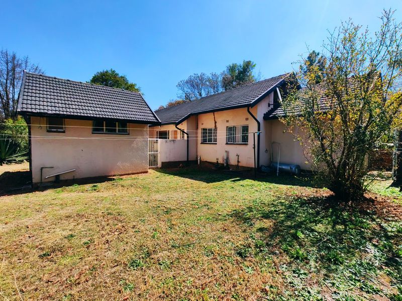 Rear view of the house showing the backyard, tiled roof, and plastered exterior walls with some visible wear and maintenance requirements.