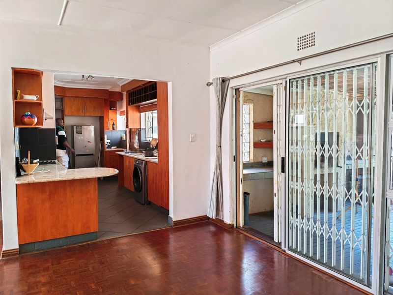 Open plan living area featuring wooden parquet flooring, flowing into a kitchen with granite countertops and wooden cabinetry, with sliding doors to the patio.