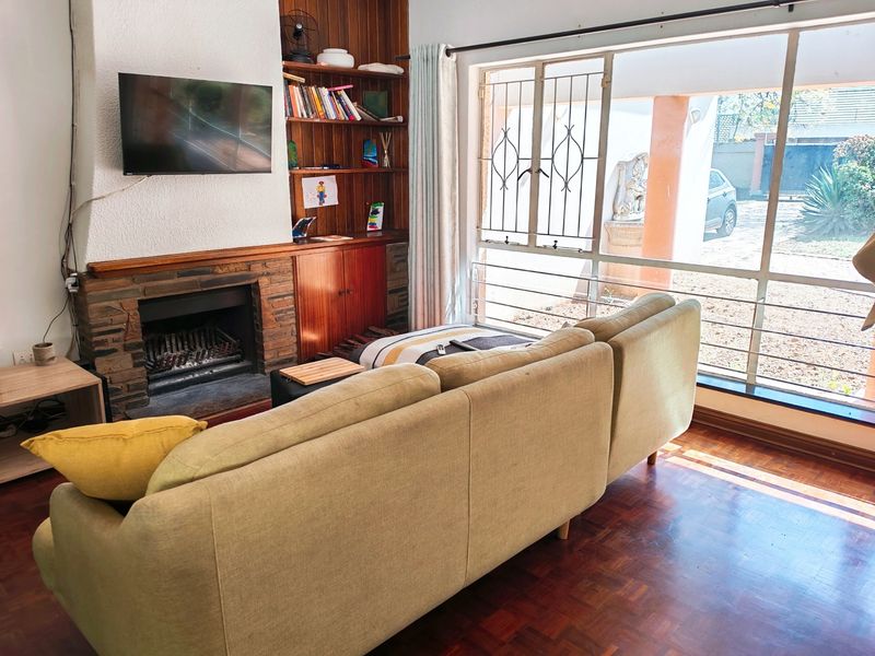 Living room featuring a stone fireplace, built-in wooden shelving, and parquet flooring, with large windows providing natural light and garden views.