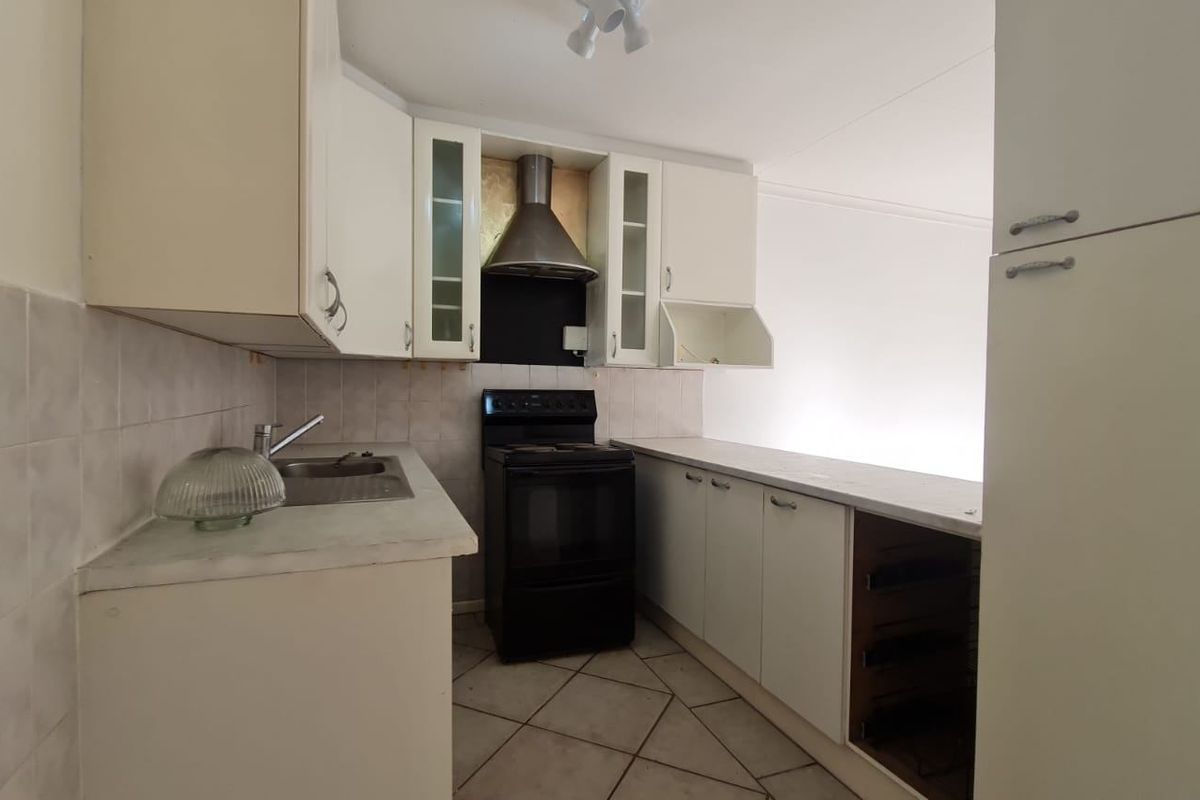 A functional kitchen featuring white cabinetry, a stainless steel extractor fan, a freestanding stove, and tiled flooring with a tiled backsplash.
