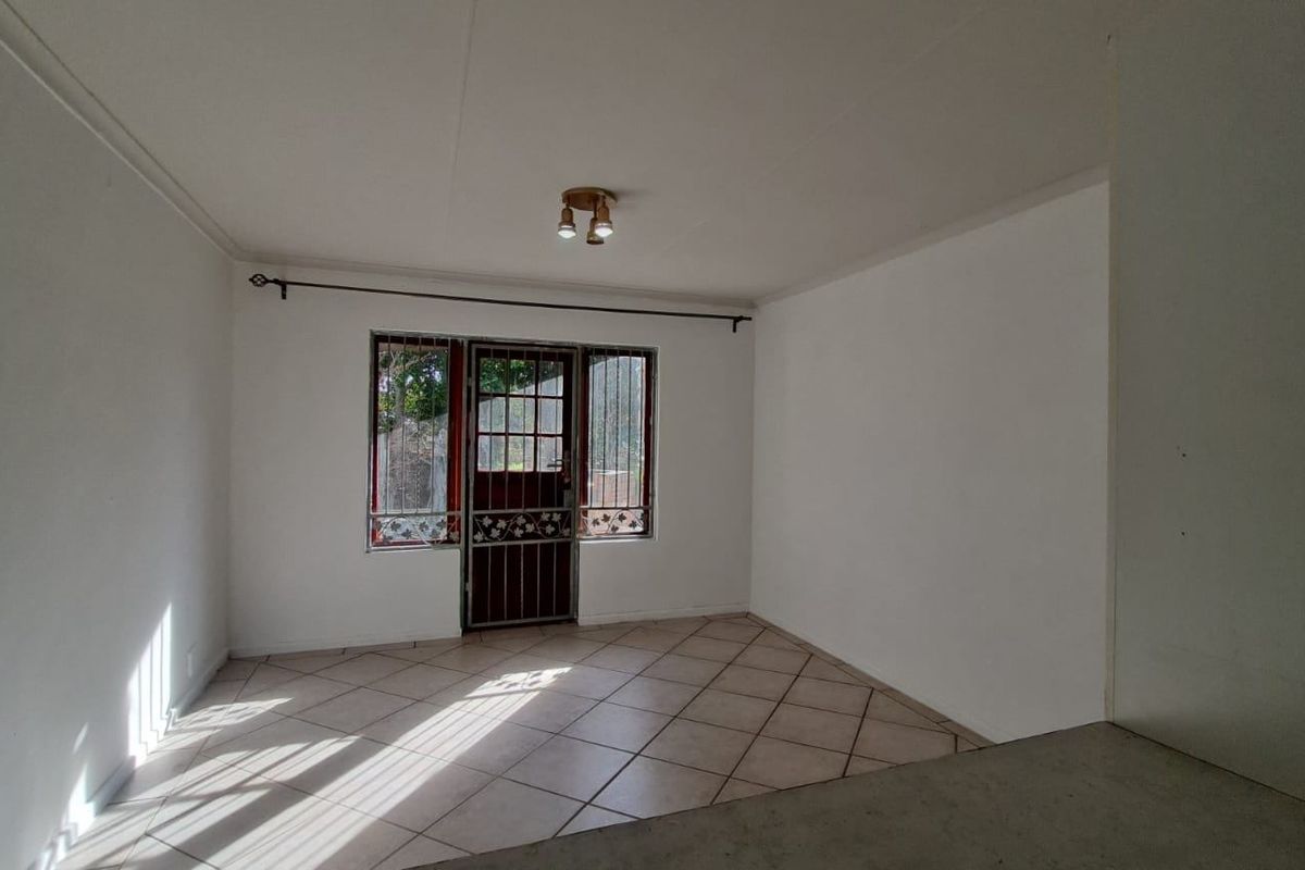 A bright, empty living area featuring tiled flooring, a security gate, and direct access to the exterior.