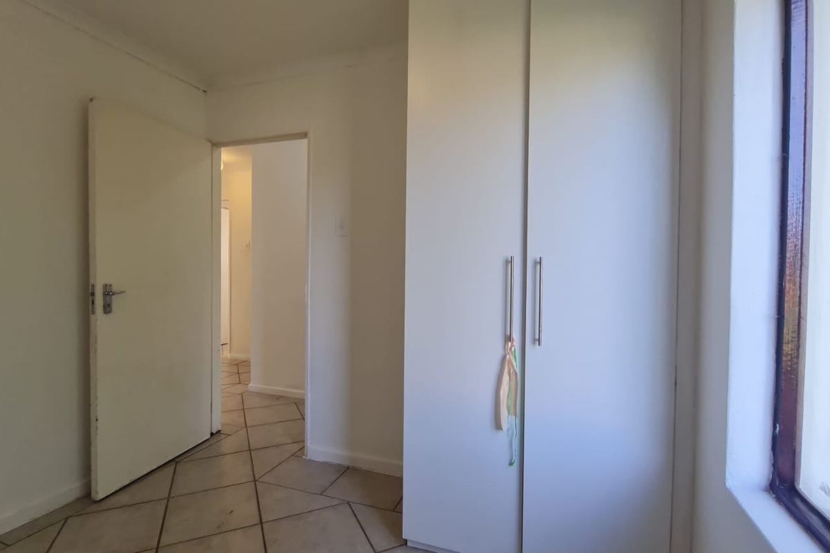 A bedroom featuring built-in cupboards, tiled flooring, and a window overlooking the garden area.