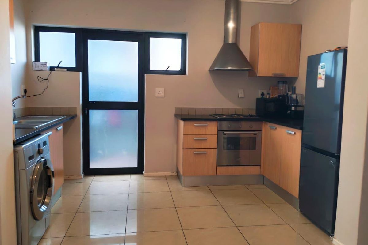 Functional kitchen featuring light wood cabinetry, dark countertops, stainless steel extractor fan, built-in oven, and tiled flooring with direct access to the exterior.