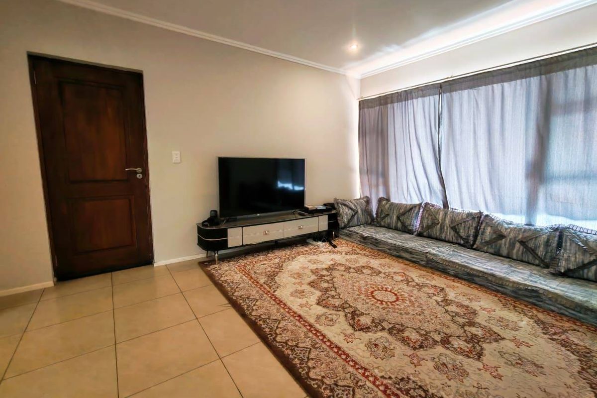 A living room featuring tiled flooring, recessed ceiling lighting, and a large window with curtaining, providing a functional and comfortable living space.