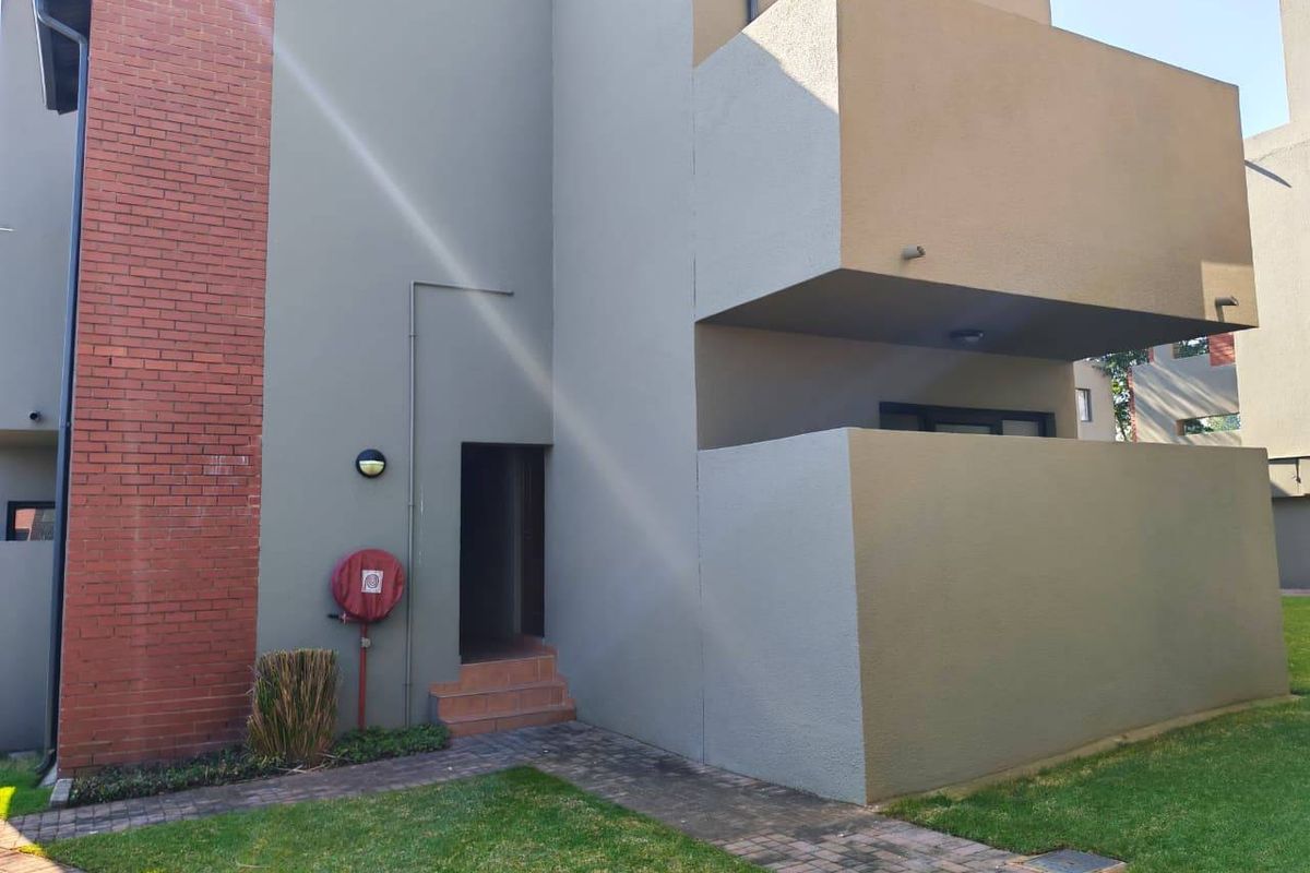 Exterior view of an apartment building featuring a brick and rendered facade, a private balcony, and a paved walkway leading to the entrance.