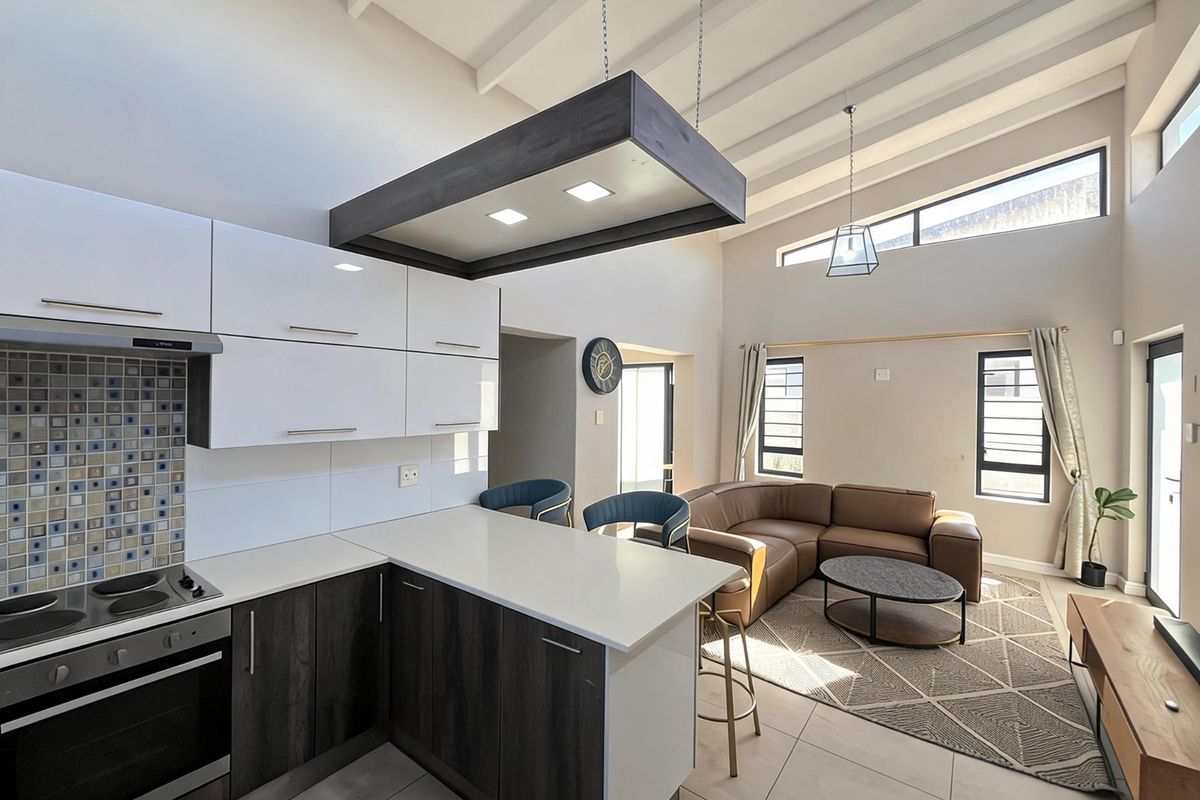Modern open-plan living area featuring a contemporary kitchen with built-in appliances, high ceilings with exposed beams, and abundant natural light from clerestory windows.