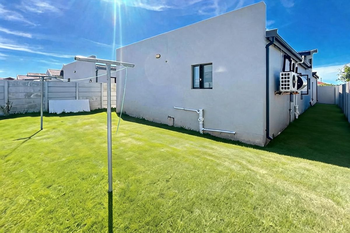 Rear exterior view of the property featuring a private lawn, boundary wall, and external air conditioning unit.