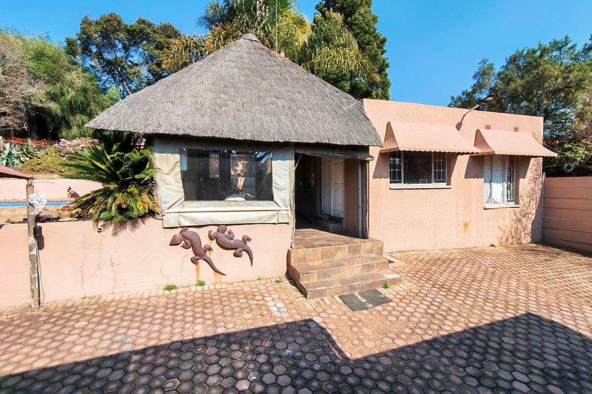 Rear exterior view featuring a thatched roof structure, paved courtyard, and metal window awnings, showing signs of weathering and maintenance needs.