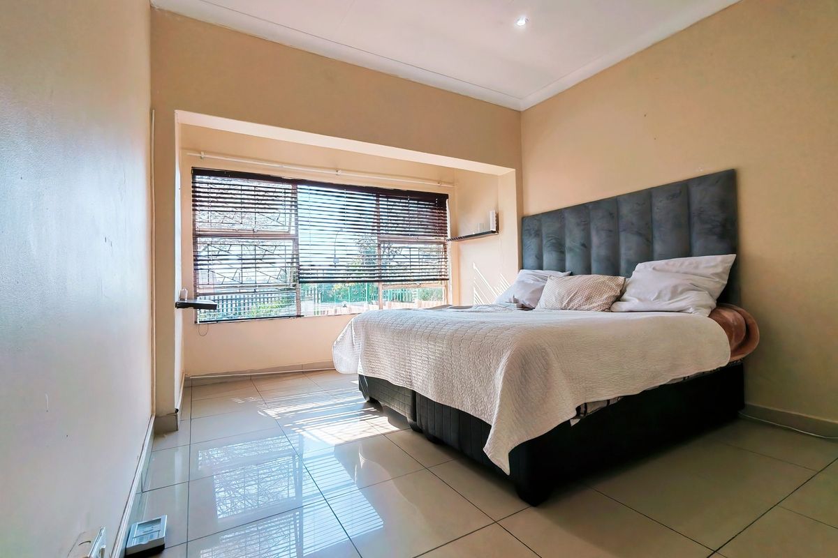 A bedroom featuring tiled flooring, a recessed window with venetian blinds, and neutral wall finishes.