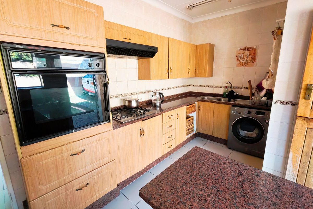 A functional kitchen featuring light wood cabinetry, granite countertops, a built-in oven, gas hob, and tiled backsplash with integrated laundry plumbing.