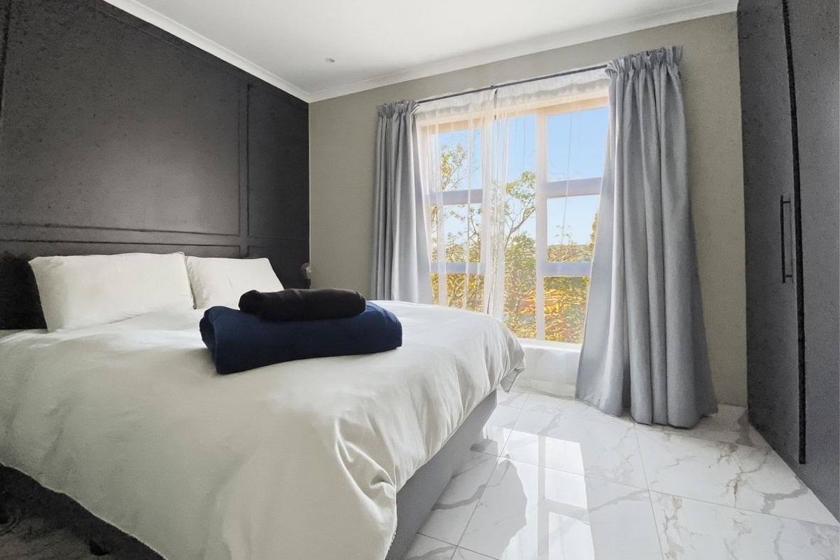 A modern bedroom featuring marble-look floor tiles, a dark feature wall with paneling, and a built-in wardrobe with natural light from the window.