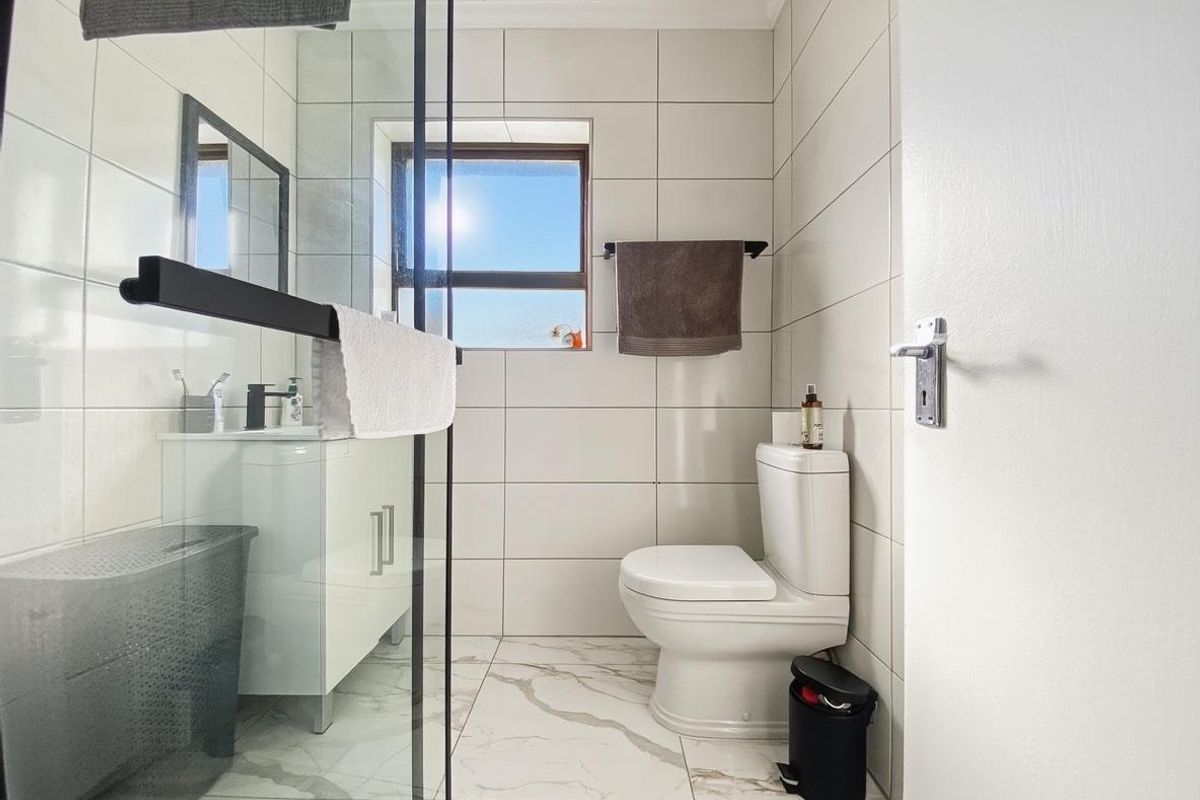 Modern bathroom featuring a glass-enclosed shower, white vanity cabinet, and neutral wall and floor tiling with a window for natural light.