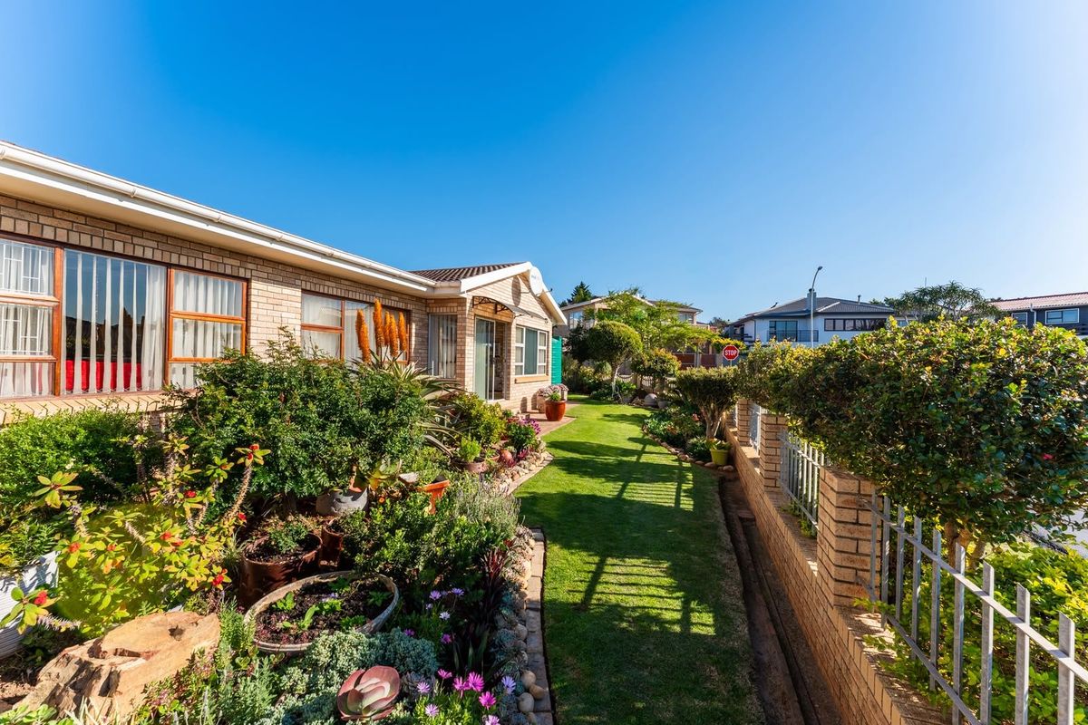 A well-maintained front garden featuring a lush lawn, established shrubbery, and a secure brick and metal perimeter fence along the property boundary.