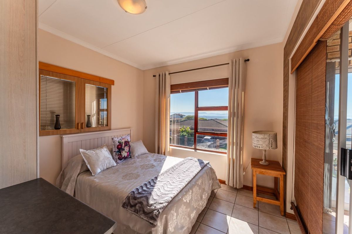 A cozy bedroom featuring tiled flooring, built-in cupboards, and a large window offering natural light and neighborhood views.