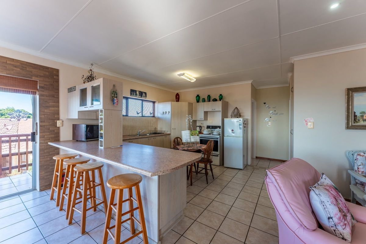 Open plan kitchen and living area featuring a breakfast bar, tiled flooring, and direct access to an outdoor balcony through a sliding glass door.