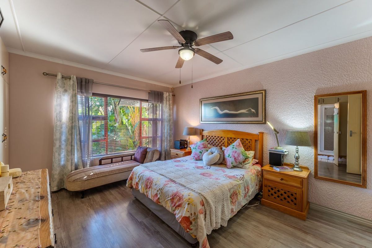 A well-lit bedroom featuring laminate flooring, a ceiling fan, and textured wall finishes, offering a comfortable and functional living space.