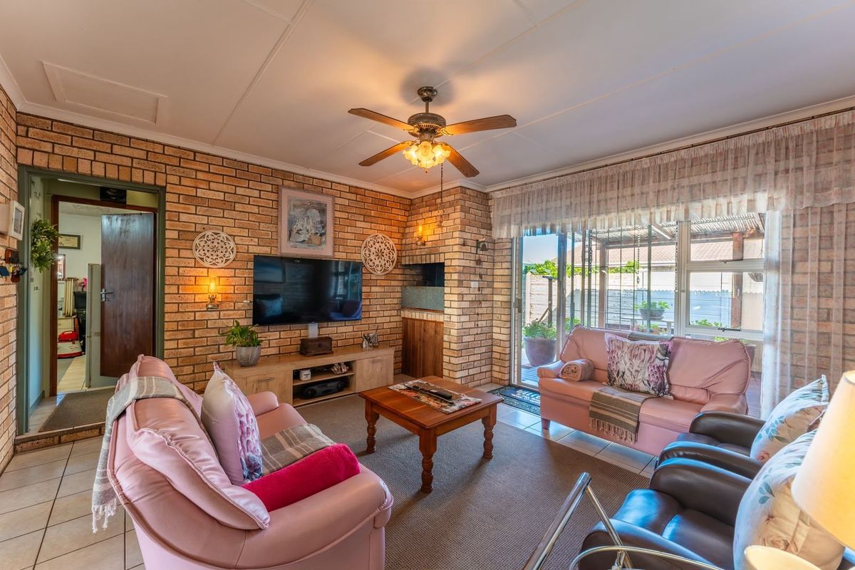 A cozy living room featuring exposed brick walls, a built-in fireplace, ceiling fan, and direct access to an outdoor patio area through sliding glass doors.