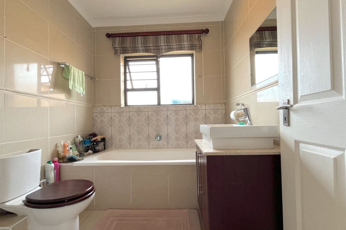 A functional bathroom featuring a built-in bathtub, a vanity cabinet with a vessel sink, and neutral wall tiling.